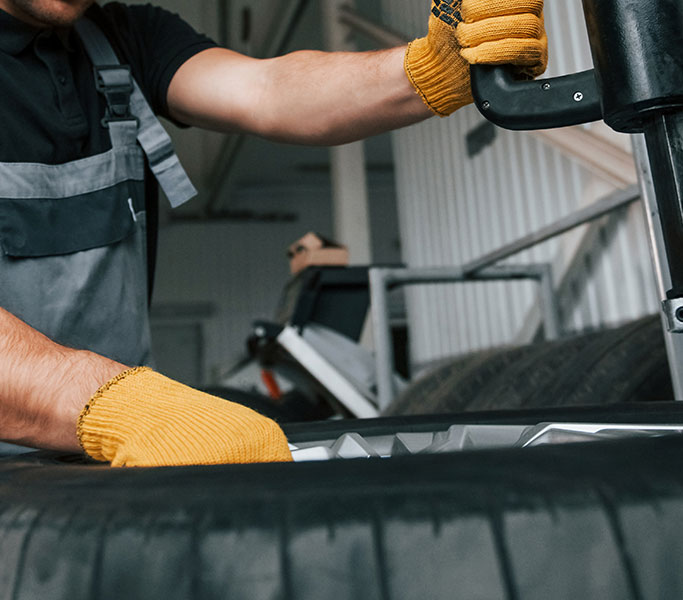 Close up view of wheel. Man in uniform is working in the auto service